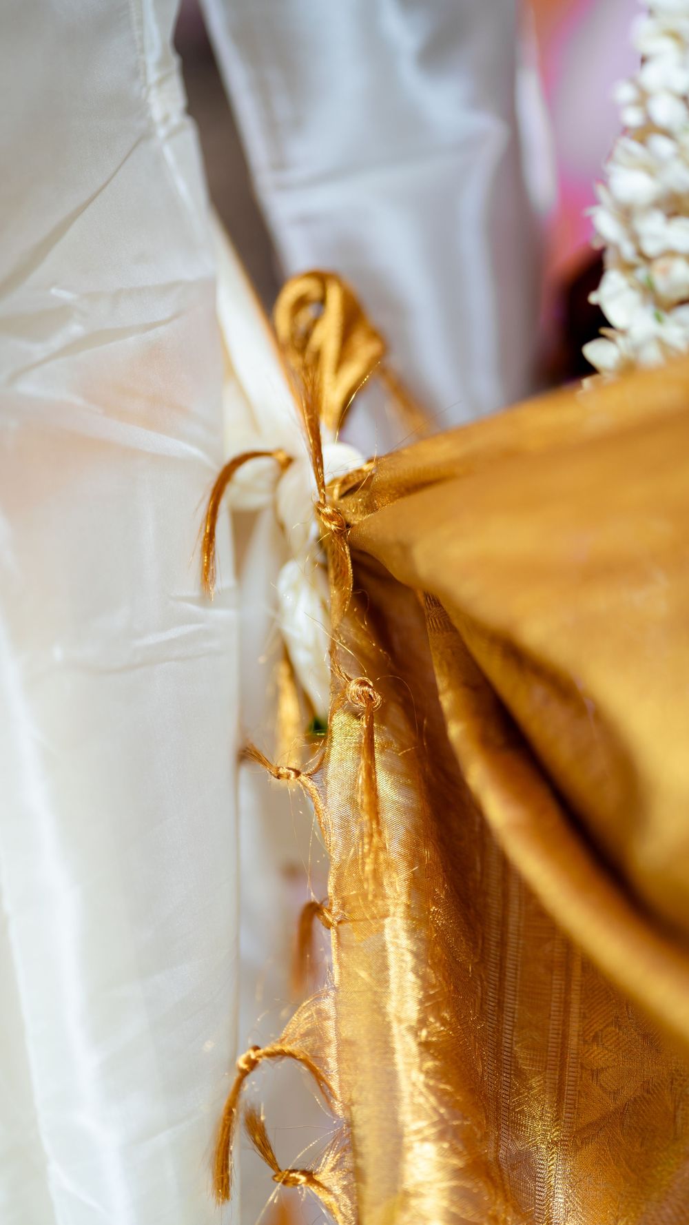 Close-up detail of gold fabric ties against white material, showing textural contrast and decorative elements.