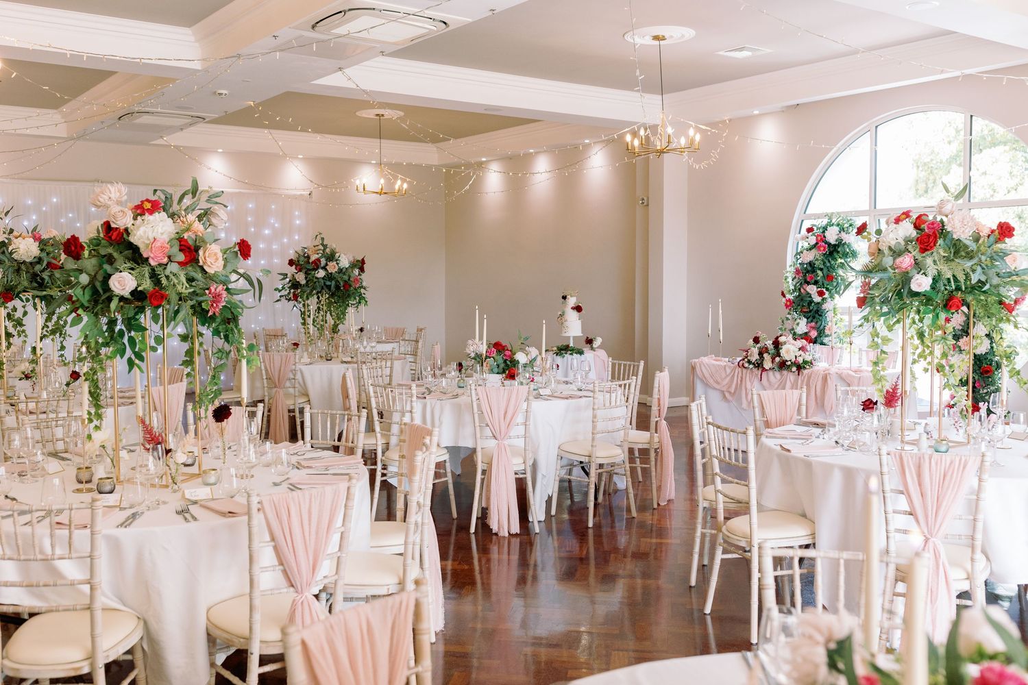 Elegant wedding reception venue with white tables, floral centerpieces, and soft pink accents in a bright modern space.