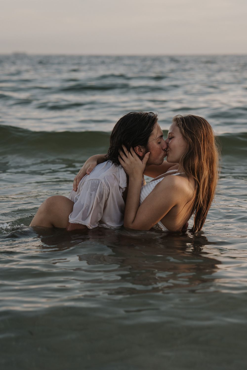 A romantic couple embraces while floating in ocean waters at sunset in upham beach, florida.