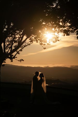 Silhouette of couple against dramatic sunset sky with mountains and trees in the background.