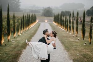 Wedding couple walking along cypress tree-lined path in romantic countryside setting.