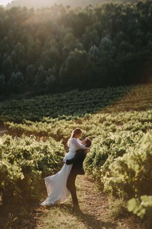 Newlyweds share an intimate moment in a sunlit vineyard at golden hour.