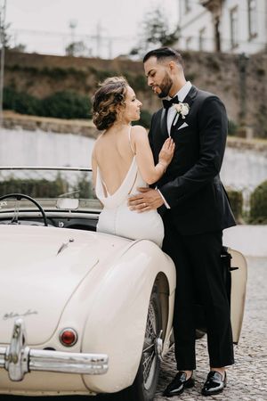 Romantic wedding portraits with a classic white vintage car against a stone backdrop.