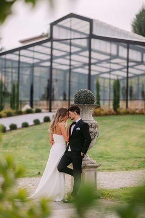 A couple shares an intimate moment under a glass greenhouse structure on their wedding day.