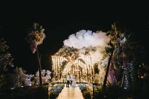 Dramatic nighttime wedding venue illuminated with string lights and palm trees.