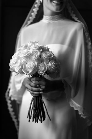 Elegant black and white photos of white rose wedding bouquet held against a bridal gown.
