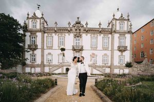 Elegant couple walking along grand historic building with ornate architecture and gardens.