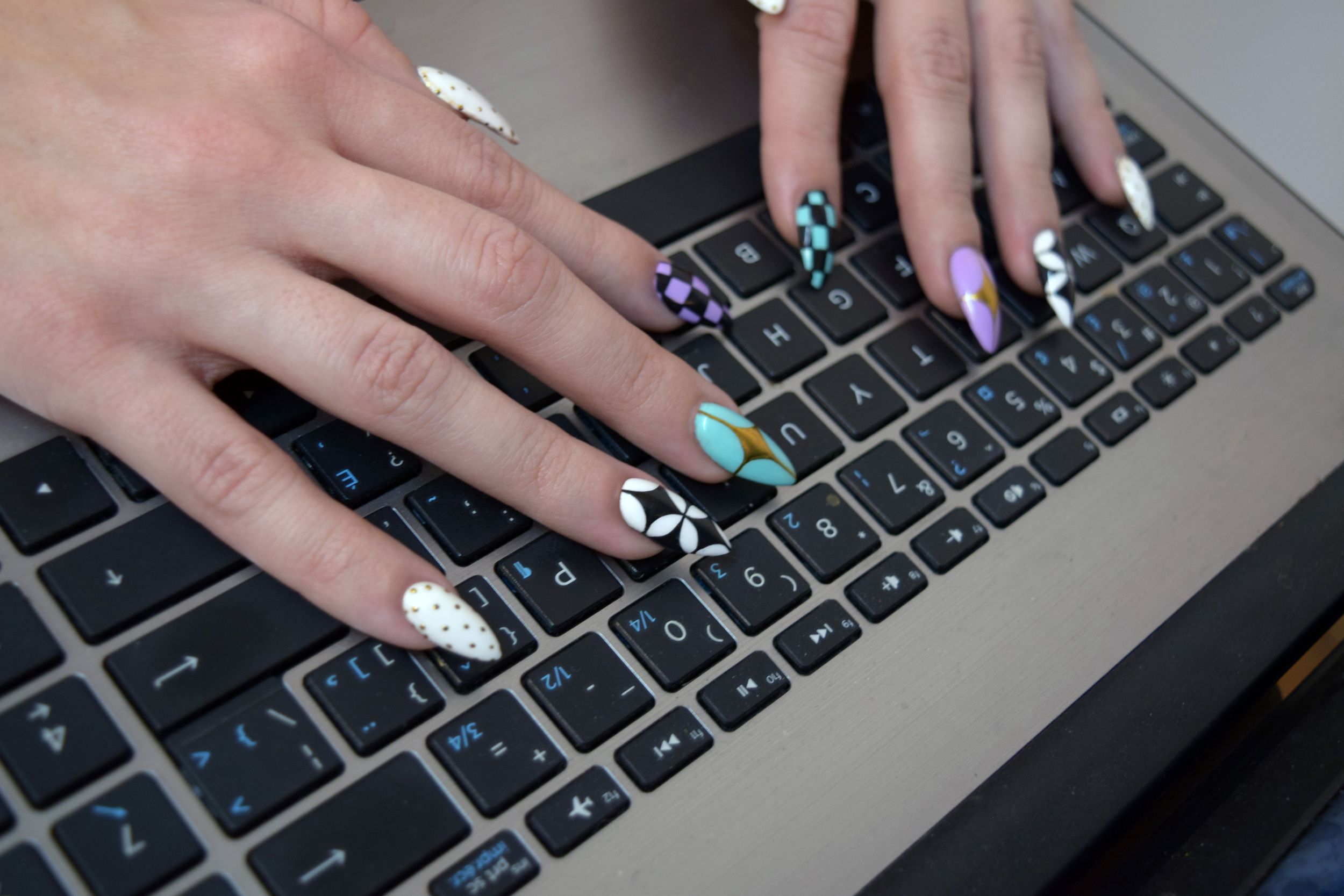 Close-up sequence showing hands with colorful nail polish typing on a laptop keyboard.