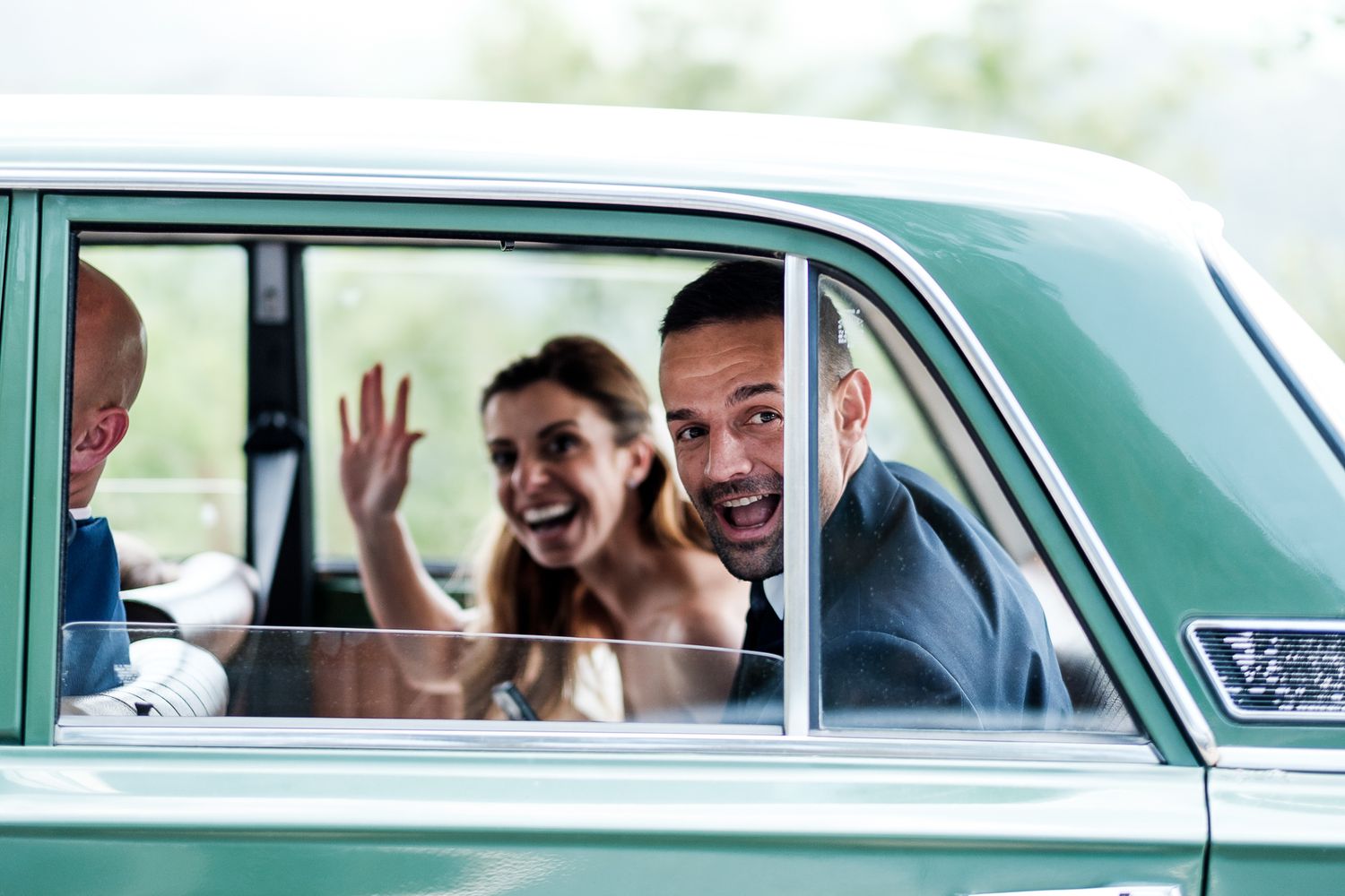 Fröhliches Brautpaar winkt aus einem Vintage-Auto: Authentische Hochzeitsreportage und pure Lebensfreude in NRW