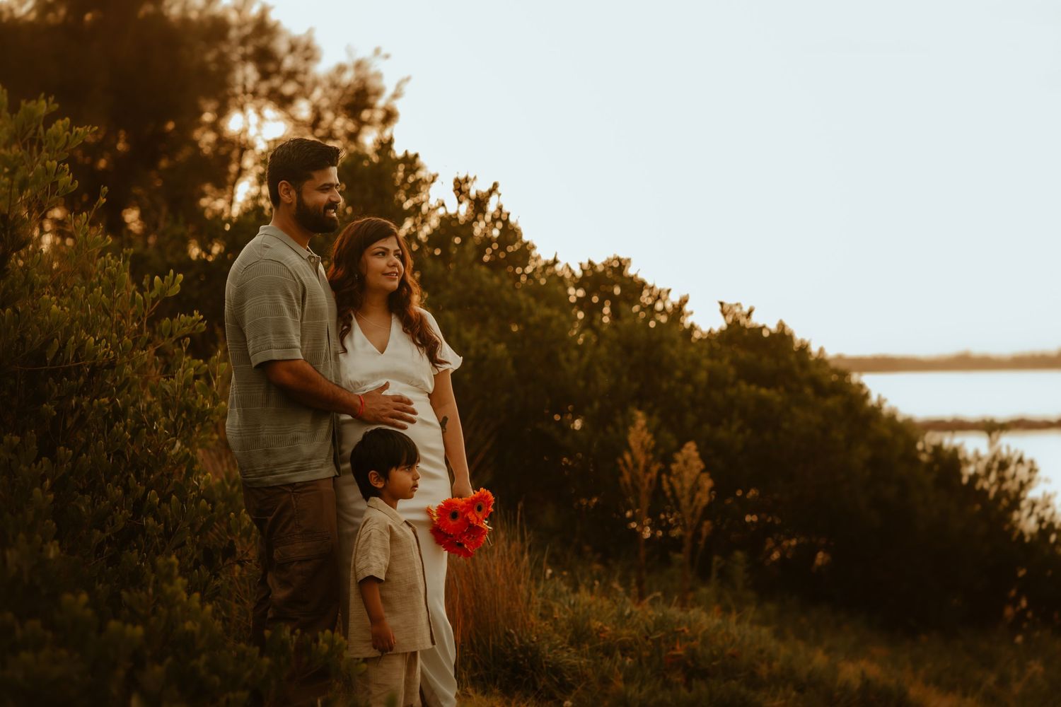 Couple embraces during golden hour sunset photoshoot by a serene waterfront with trees in the background In Cronulla NSW