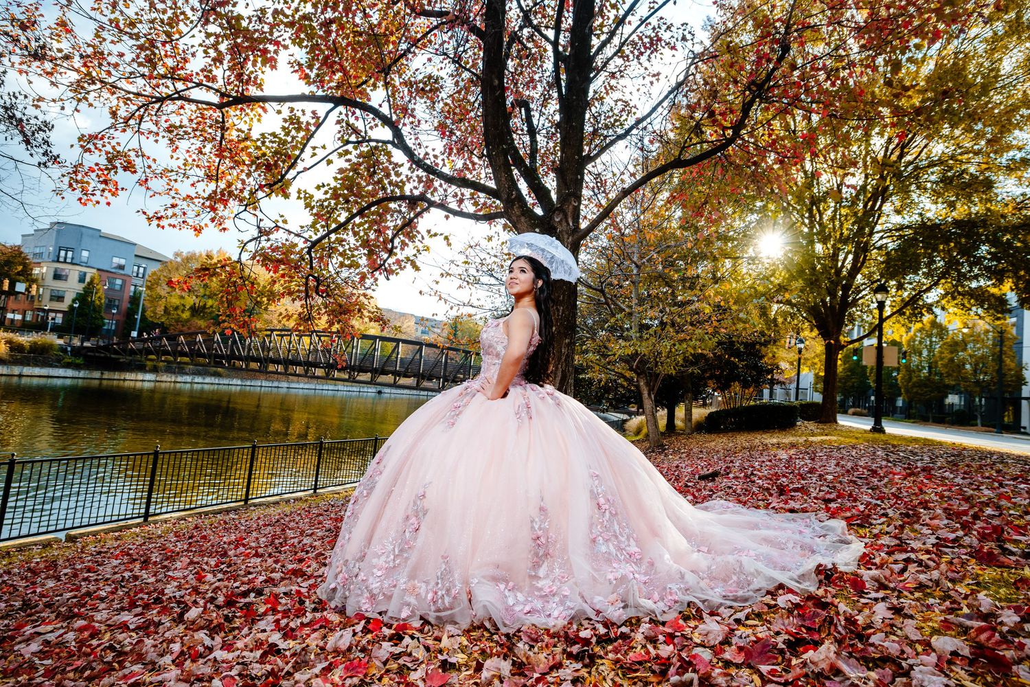 A pink ballgown dress flows elegantly among scattered autumn leaves in a scenic outdoor setting during golden hour.