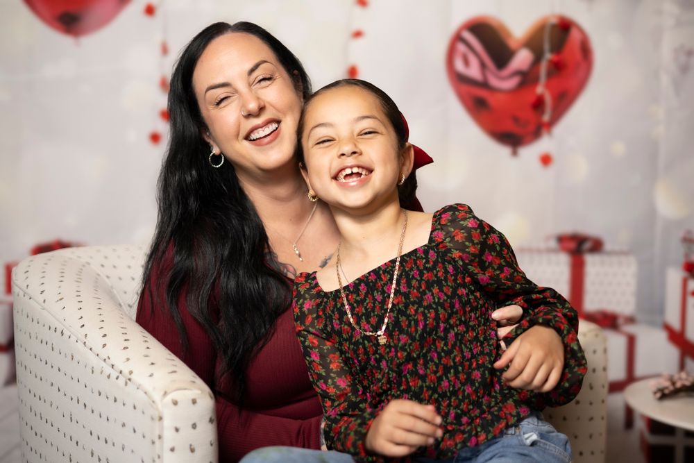 Two people share a joyful moment together against a backdrop decorated with red heart balloons.