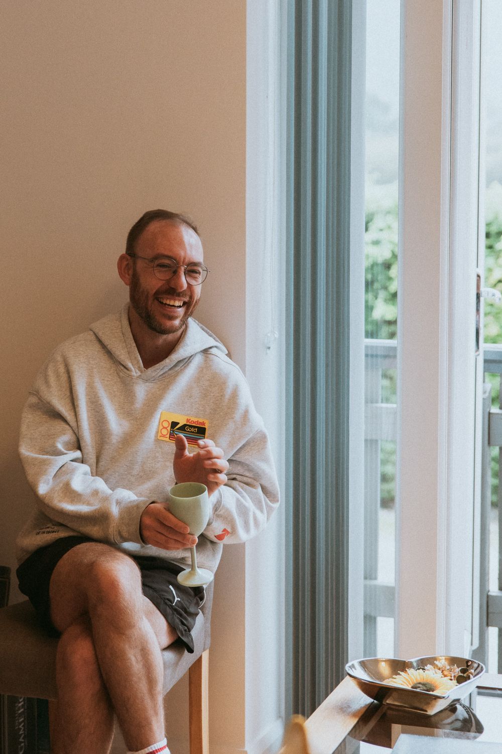 Person in grey hoodie sitting by window enjoying coffee and snacks.