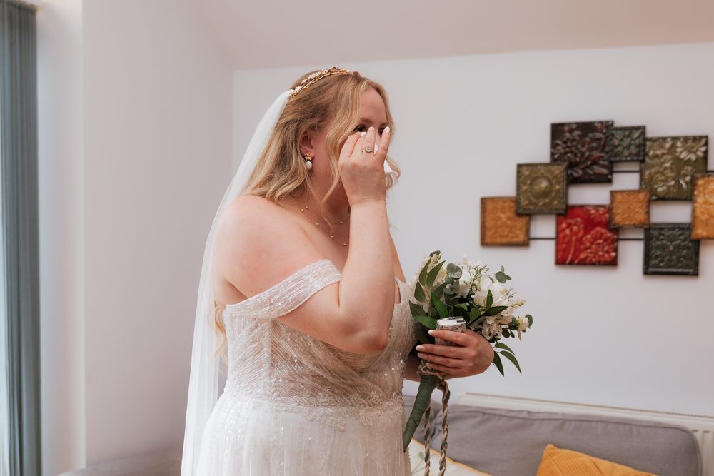 An emotional wedding moment captured in a light-filled room with decorative wall art.