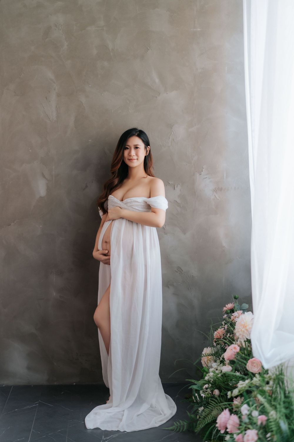 Ethereal bridal portraits in soft white fabric against textured gray wall with delicate pink floral arrangements.飄逸的新娘肖像照，身穿柔和的白色面料，背景是紋理豐富的