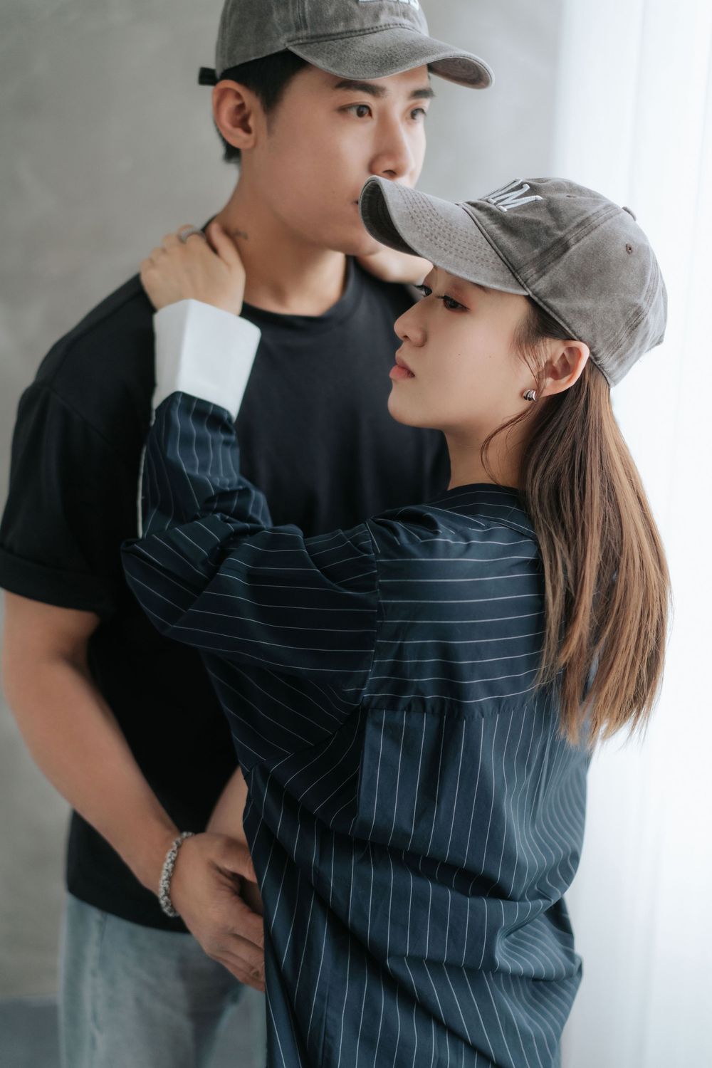 A couple wearing baseball caps and casual attire share intimate moments in a series of romantic poses against a gray wall.一對戴著棒球帽、穿著休閒裝的情侶