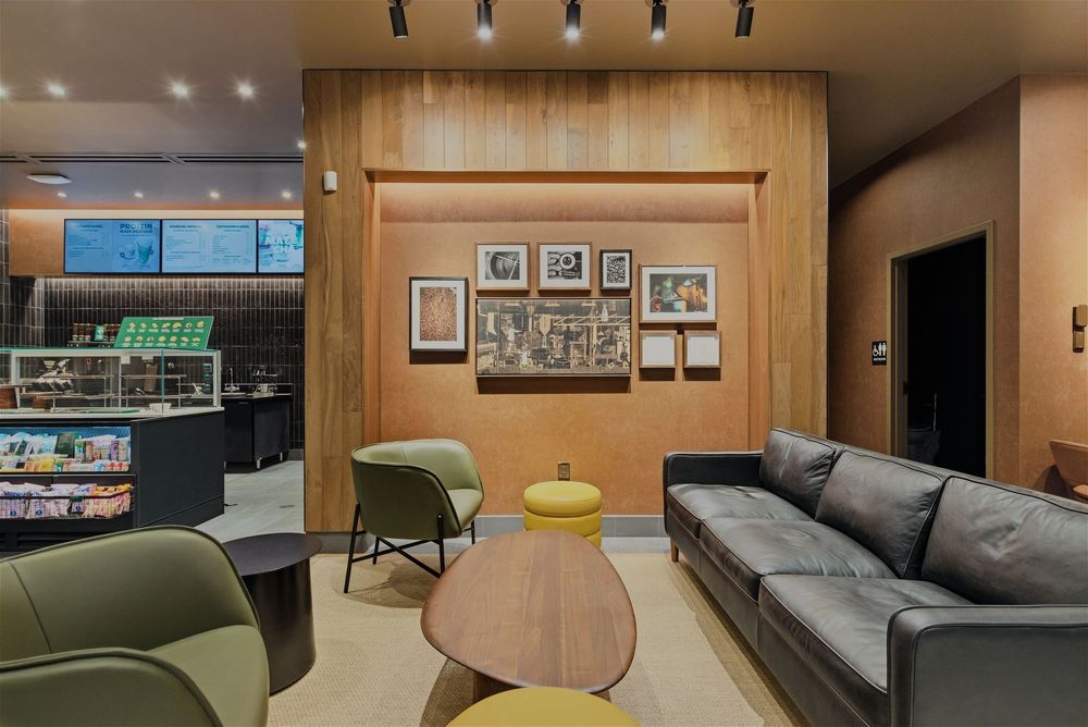 Contemporary office break room with grey sectional sofa, wooden accents, and minimalist decor.