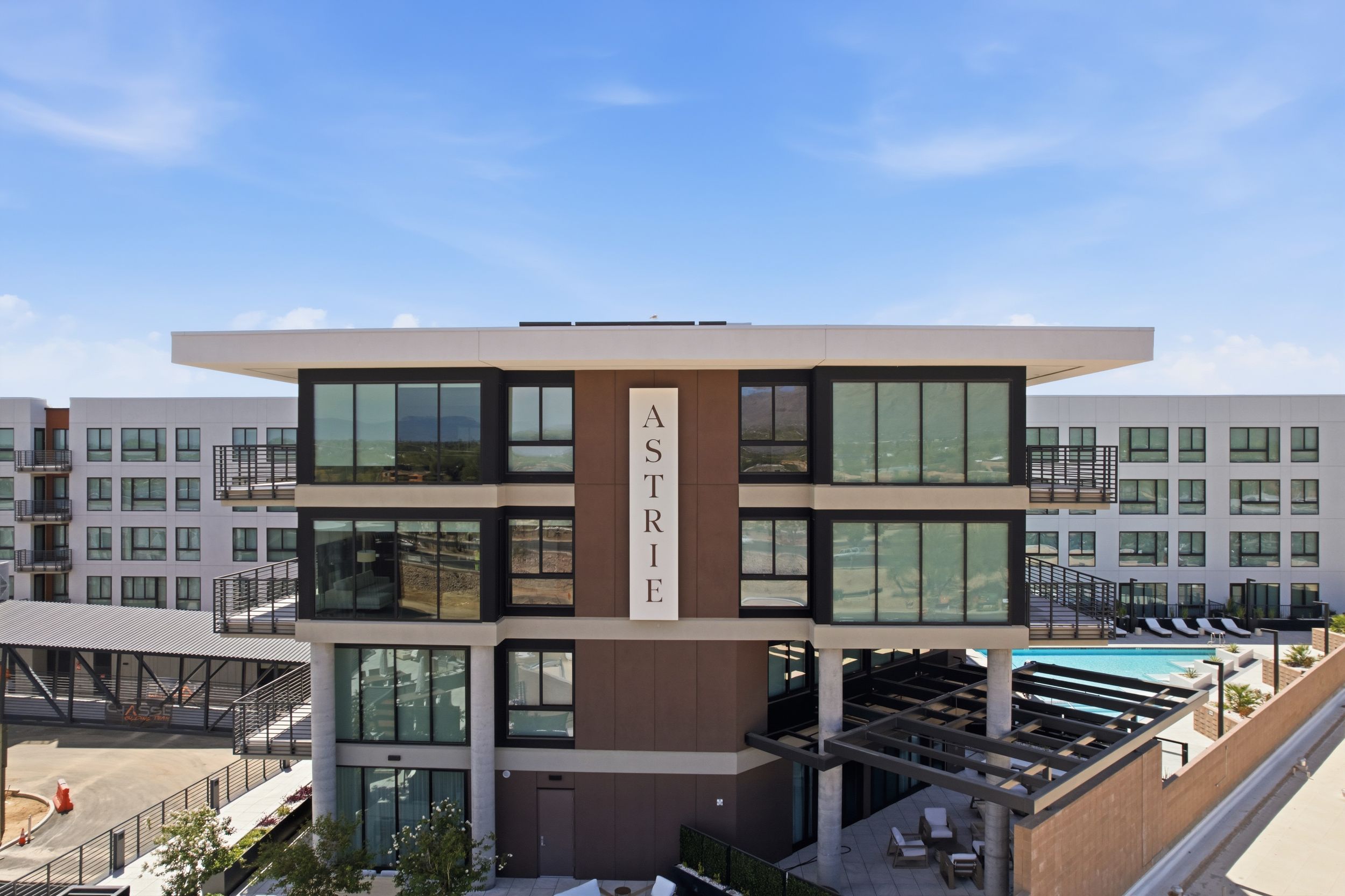 Astrie luxury apartment building exterior with pool area and clear blue sky.