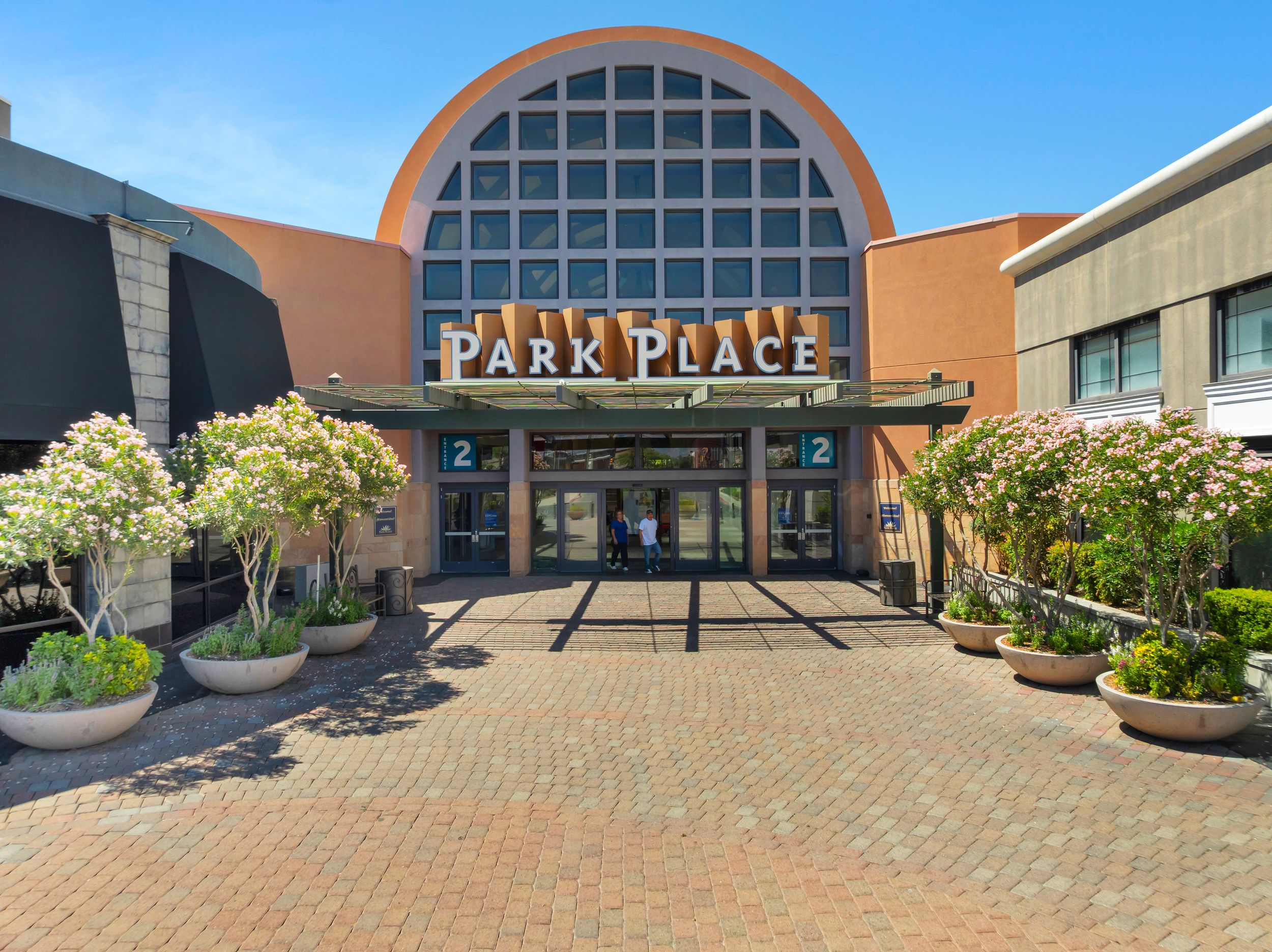 Exterior entrance of Park Place mall featuring a large arched window, brick facade, potted plants, and a paved courtyard.