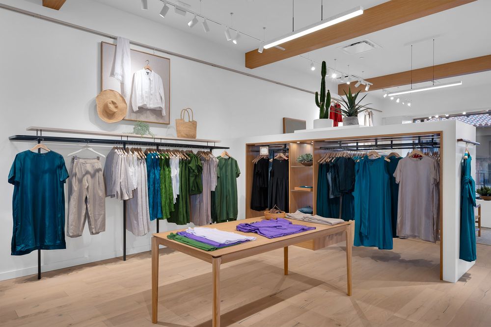 Modern clothing boutique with colorful apparel on wooden racks, folded garments on display table, and cactus decor.