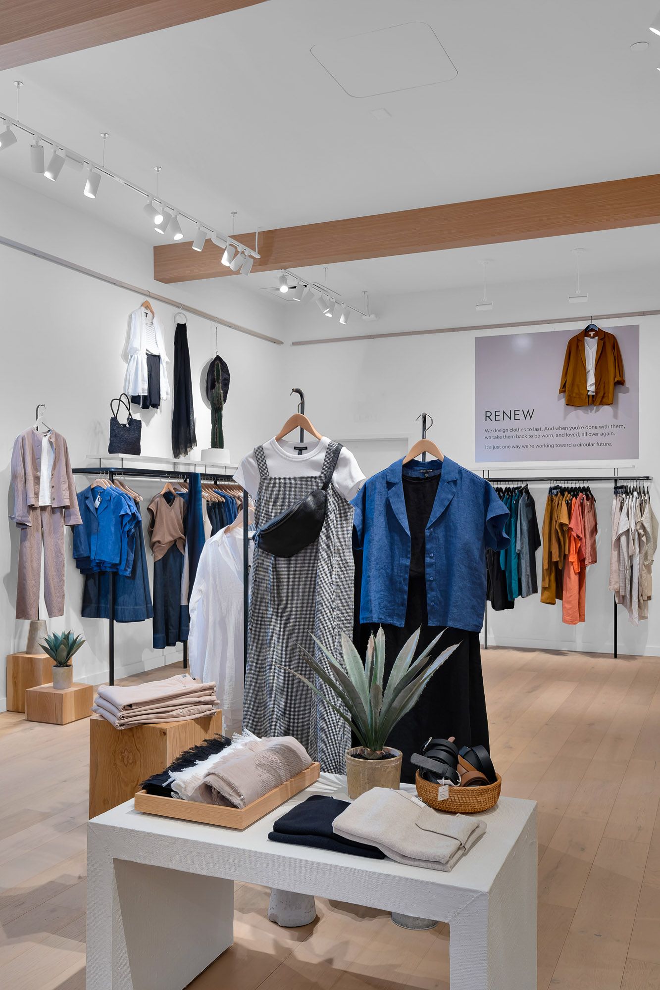 Modern boutique clothing store interior with colorful apparel on racks, folded items on white tables, and a Renew sign.
