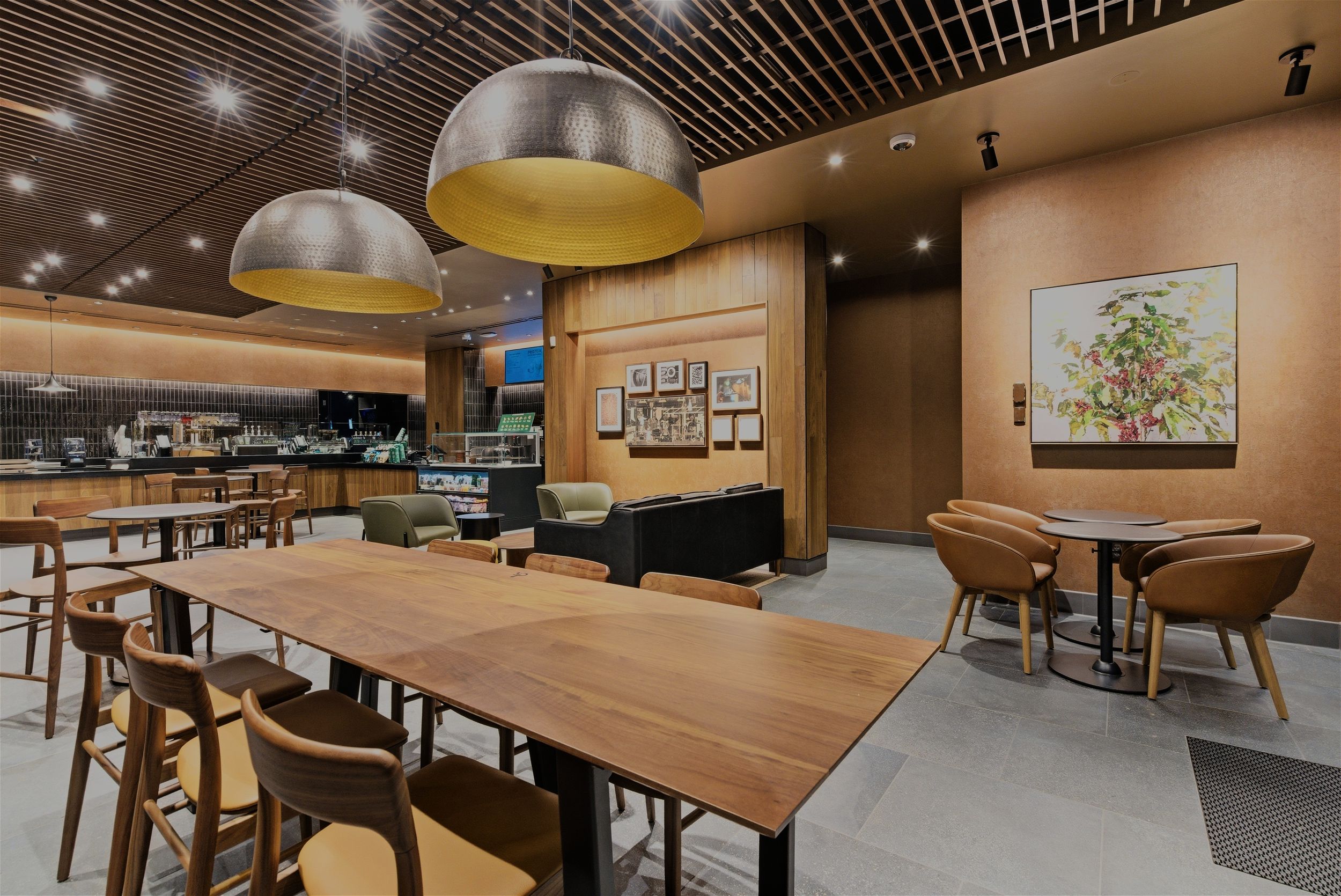 Modern cafe interior with wooden tables, large dome pendant lights, and artwork on salmon-colored walls.