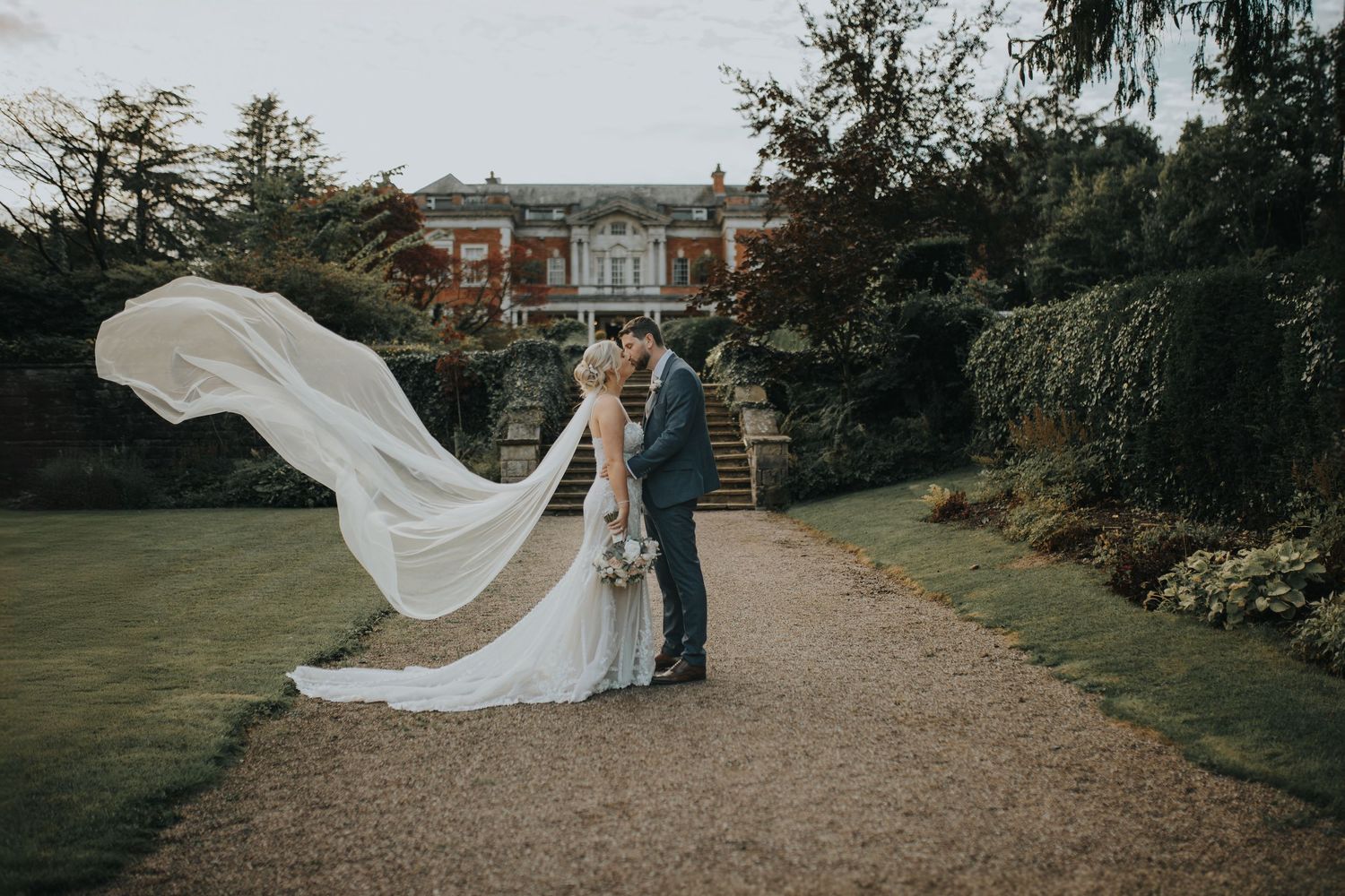 bride and groom kiss in front of eaves hall in Clitheroe, ribble valley with veil blowing in the breeze behind the bride.