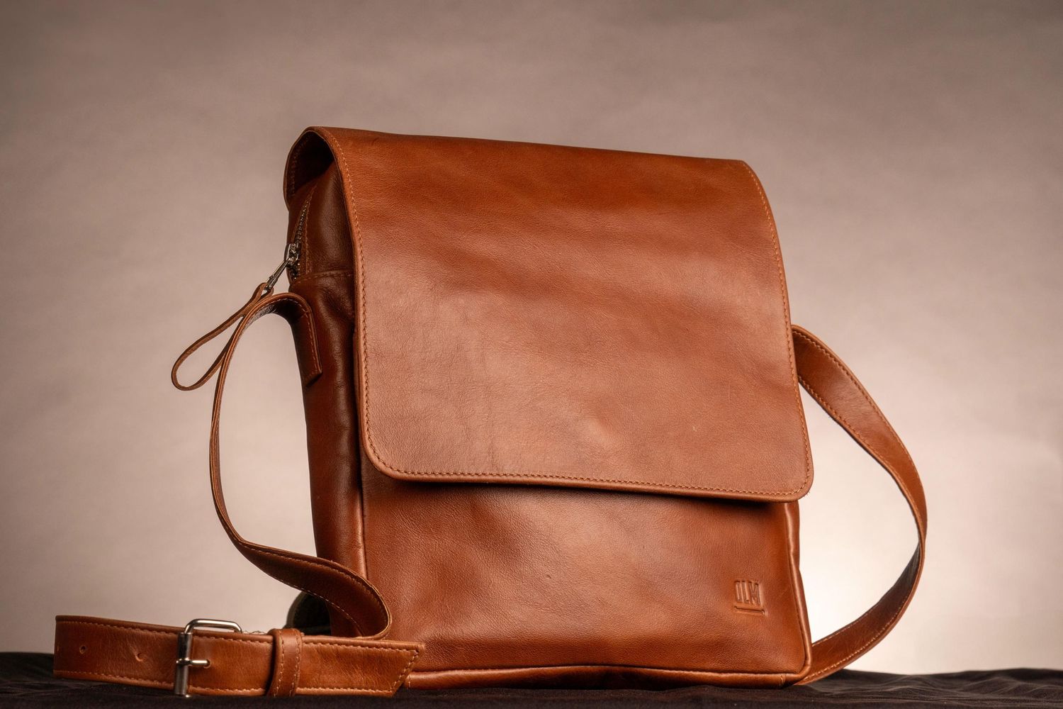 Bolso mensajero de cuero marrón estilo vintage sobre fondo neutro.