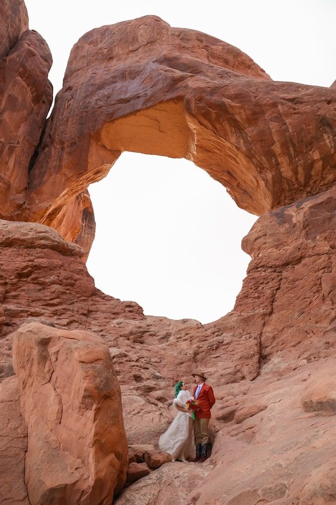 Natural stone arch formation in Arches National Park with visitors providing scale beneath the curved rock.