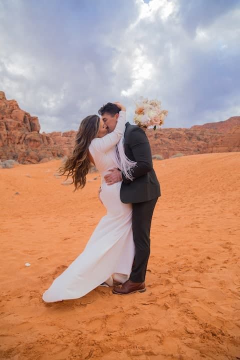 Newlywed couple shares romantic moments on red desert sand dunes during their wedding photo session.