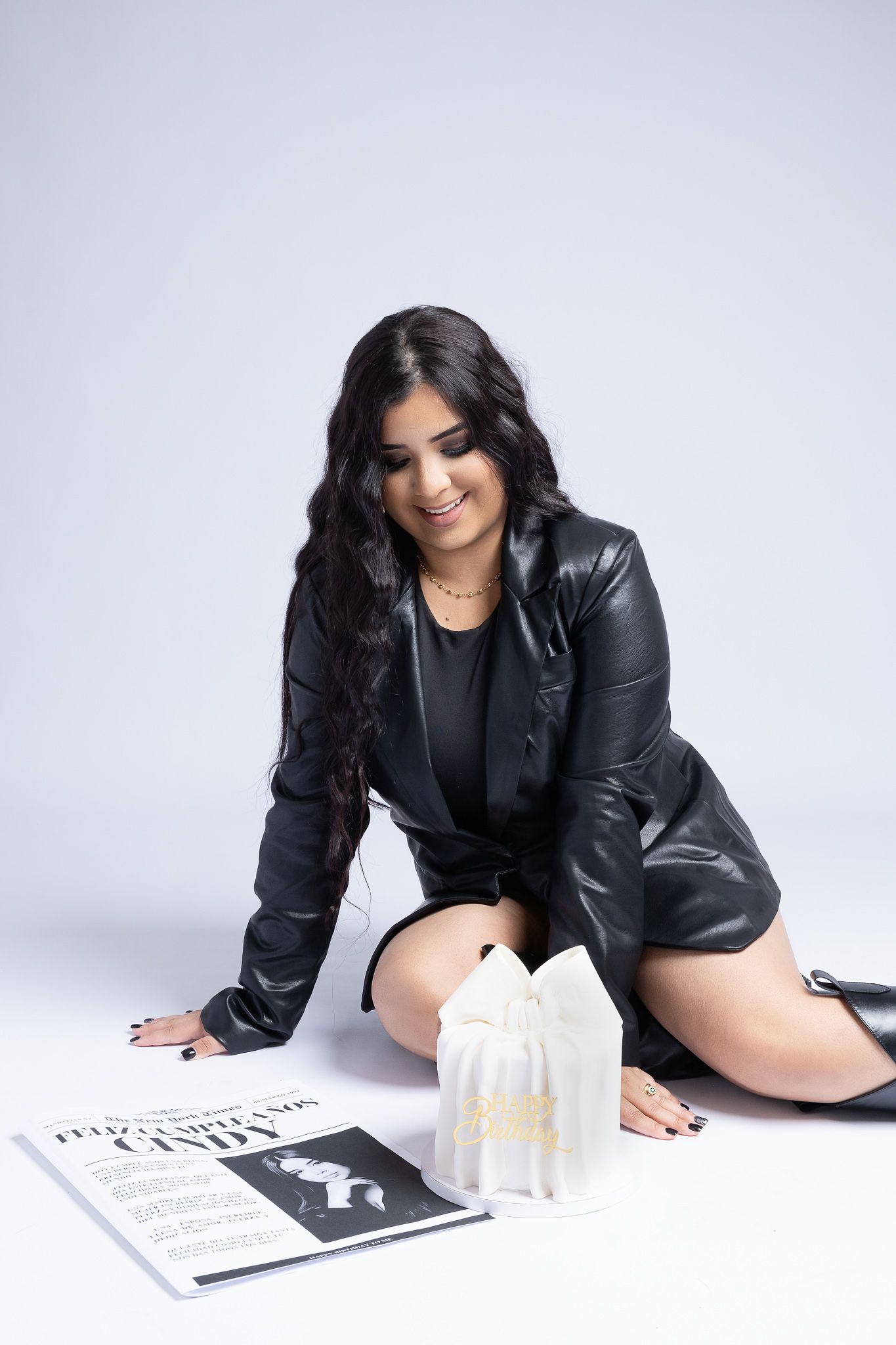 A woman in black leather jacket poses on the floor with a magazine and candles.