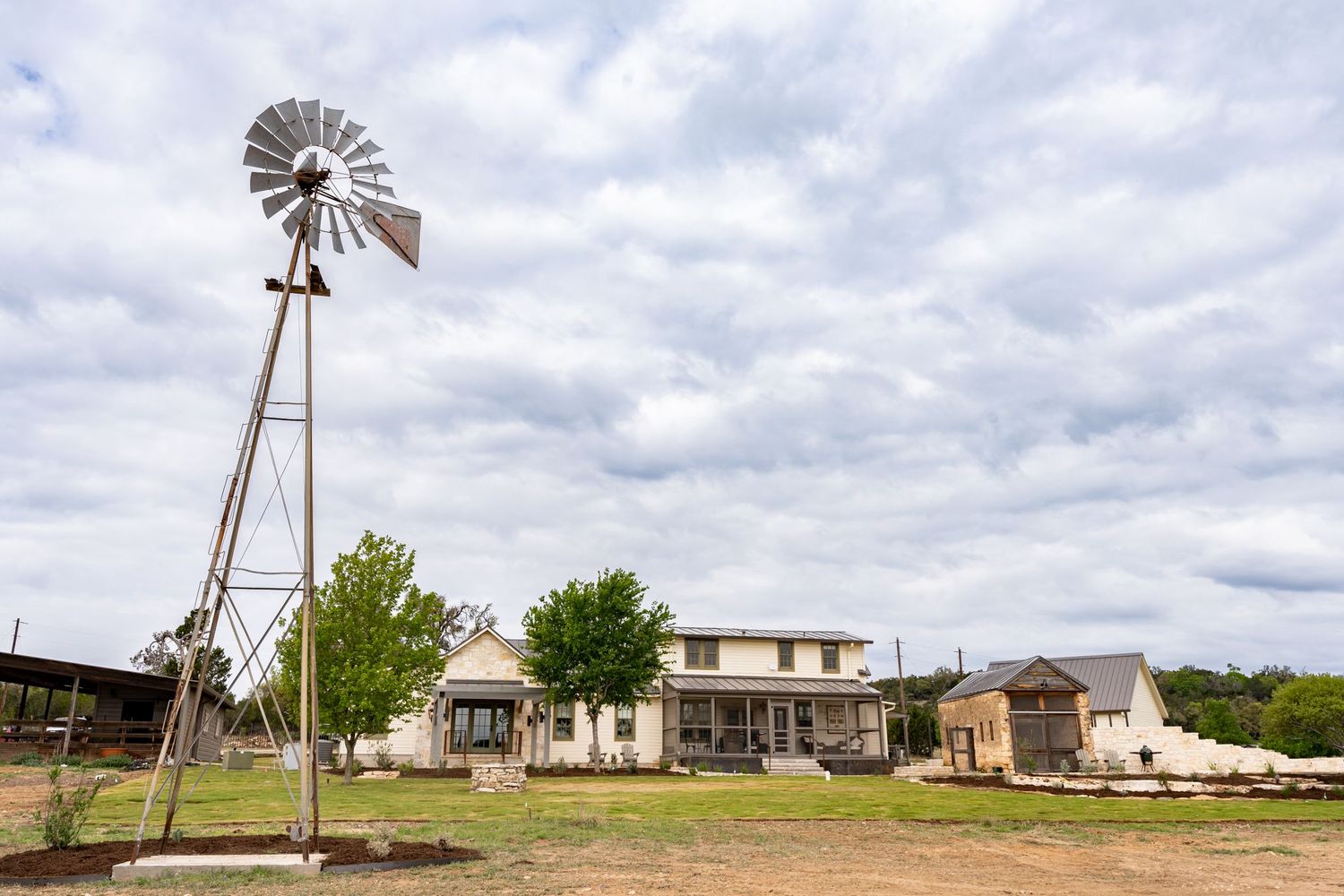 Panoramic view of a rustic ranch property with windmills and outbuildings under cloudy Texas skies.