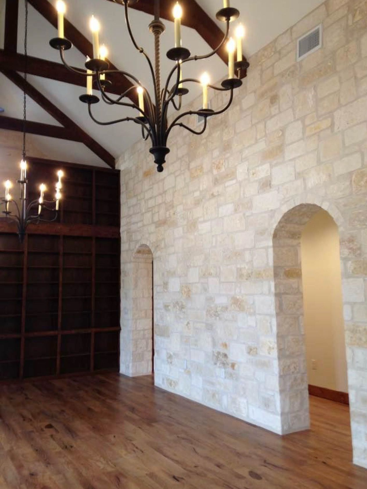 Interior space with vaulted ceiling, stone walls, and rustic wood beams with chandelier lighting.