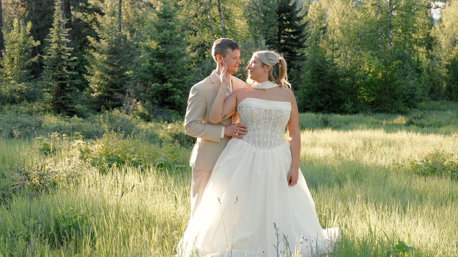 A couple exchanges wedding vows under a floral arch decorated with white roses and greenery during an outdoor ceremony.