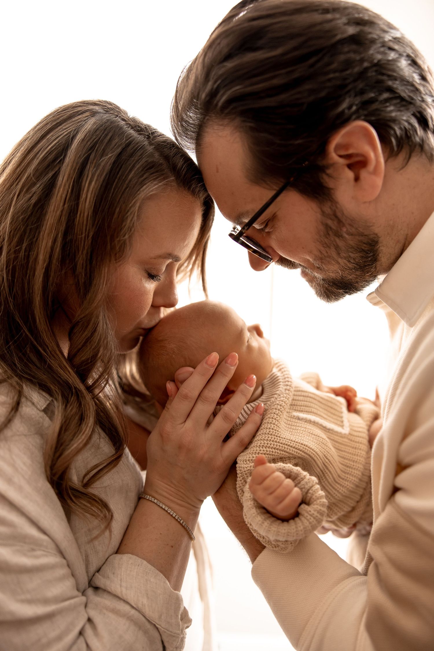 Mom and dad sitting on a couch at home admiring their newborn baby and holding his tiny hand during an in-home session in Central Indiana.