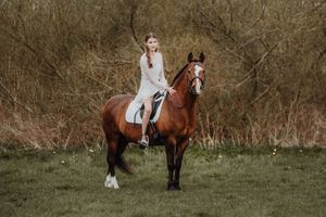 Young woman in white dress riding a chestnut horse in a natural outdoor setting.