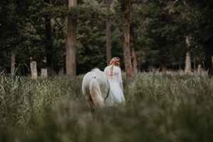 A romantic couple embraces in a sunlit meadow surrounded by tall grass and trees during a summer afternoon.