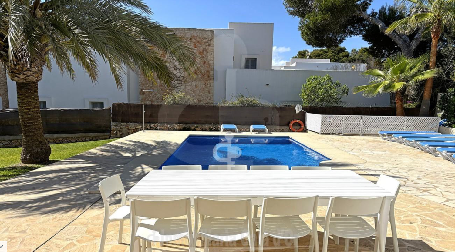 Sparkling blue swimming pool with lounge chairs lined up along the stone deck on a sunny day.