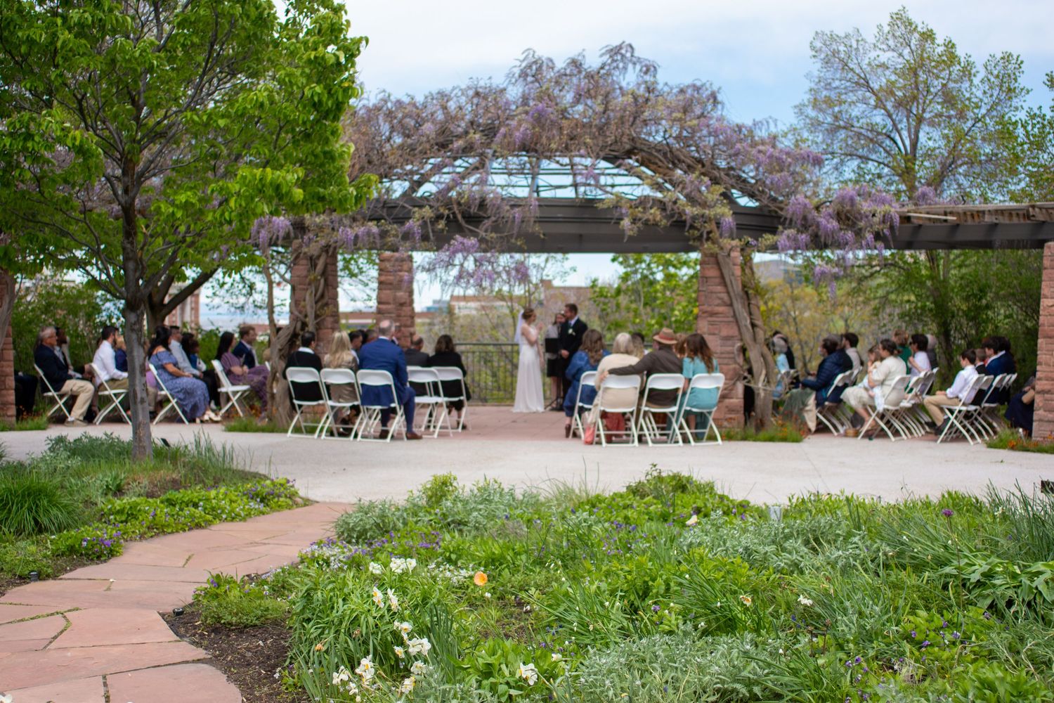 Wedding guests gather around a table during an outdoor reception at a rustic venue.