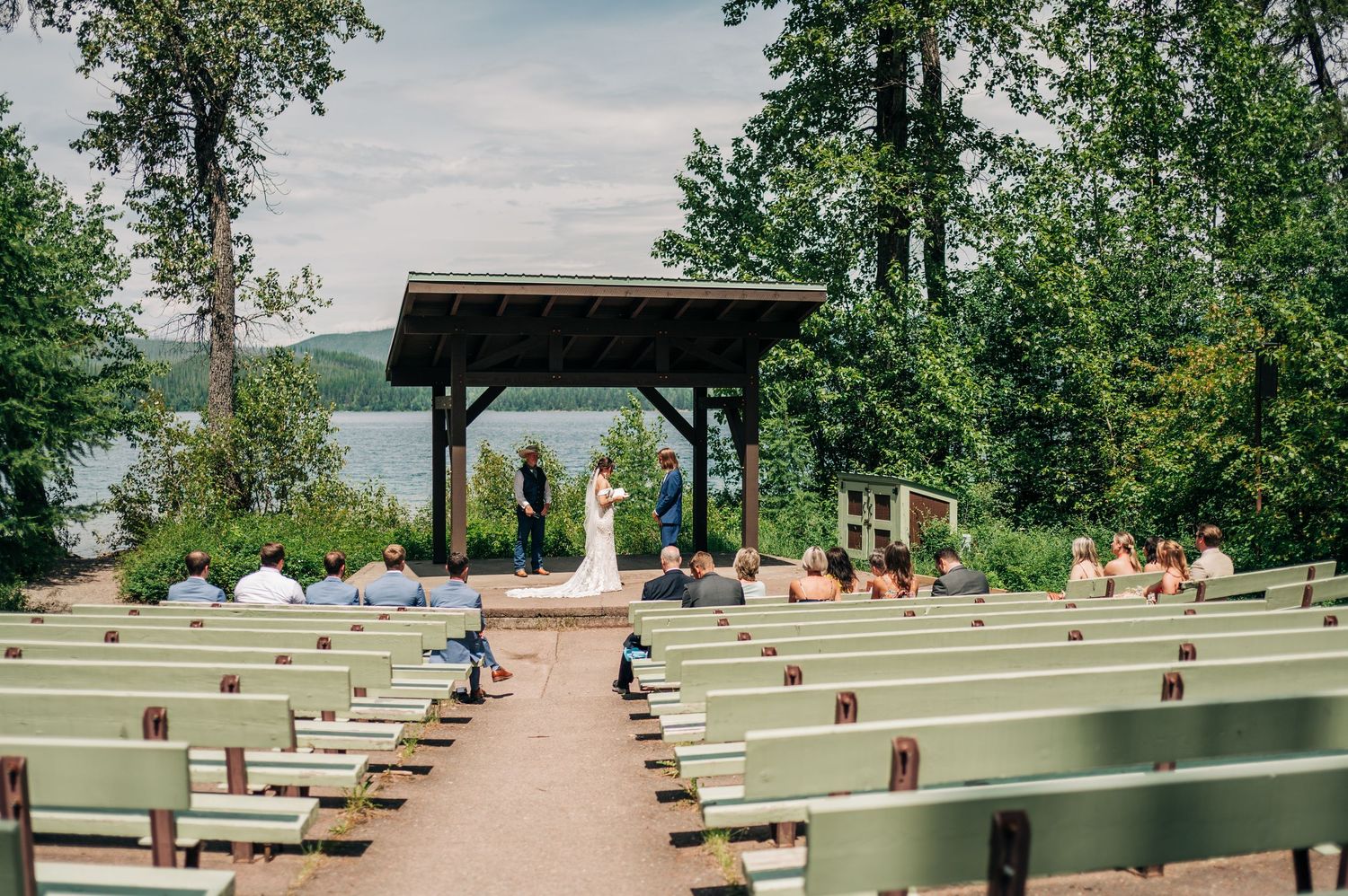 Outdoor wedding ceremony setup with green benches and covered gazebo overlooking a scenic natural landscape.