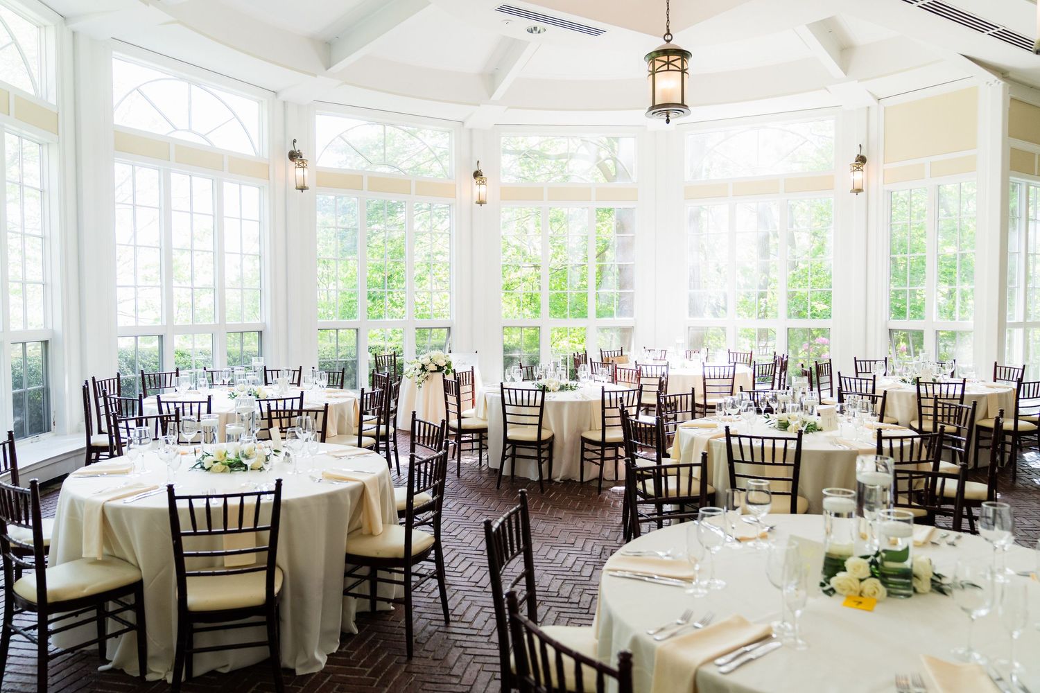 Elegant wedding reception at Tupper Manor in Beverly, MA with white tables, dark chiavari chairs, and sunlit windows.