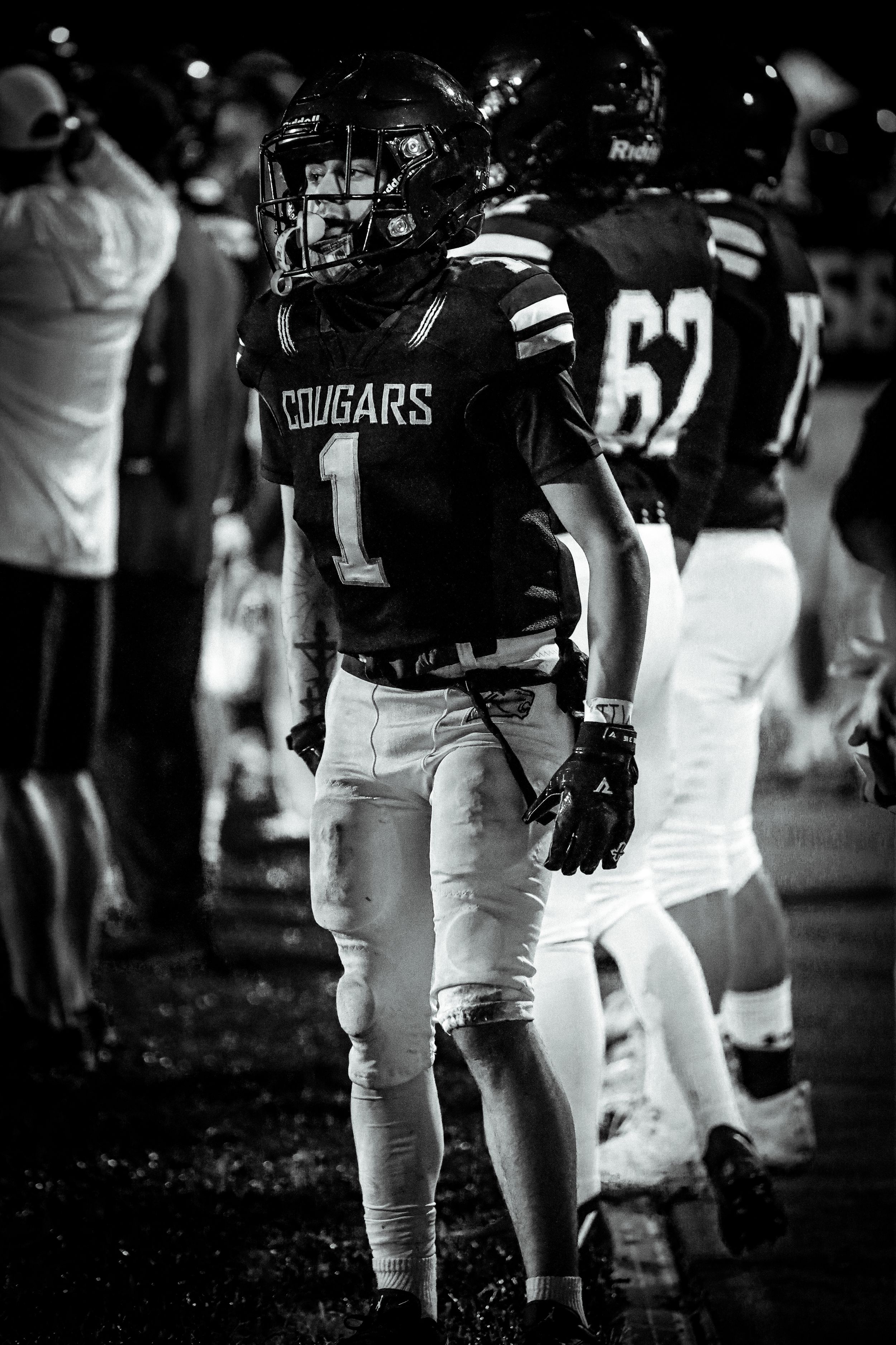 Black and white photo of Cougars football player number 1 standing on sideline during night game.
