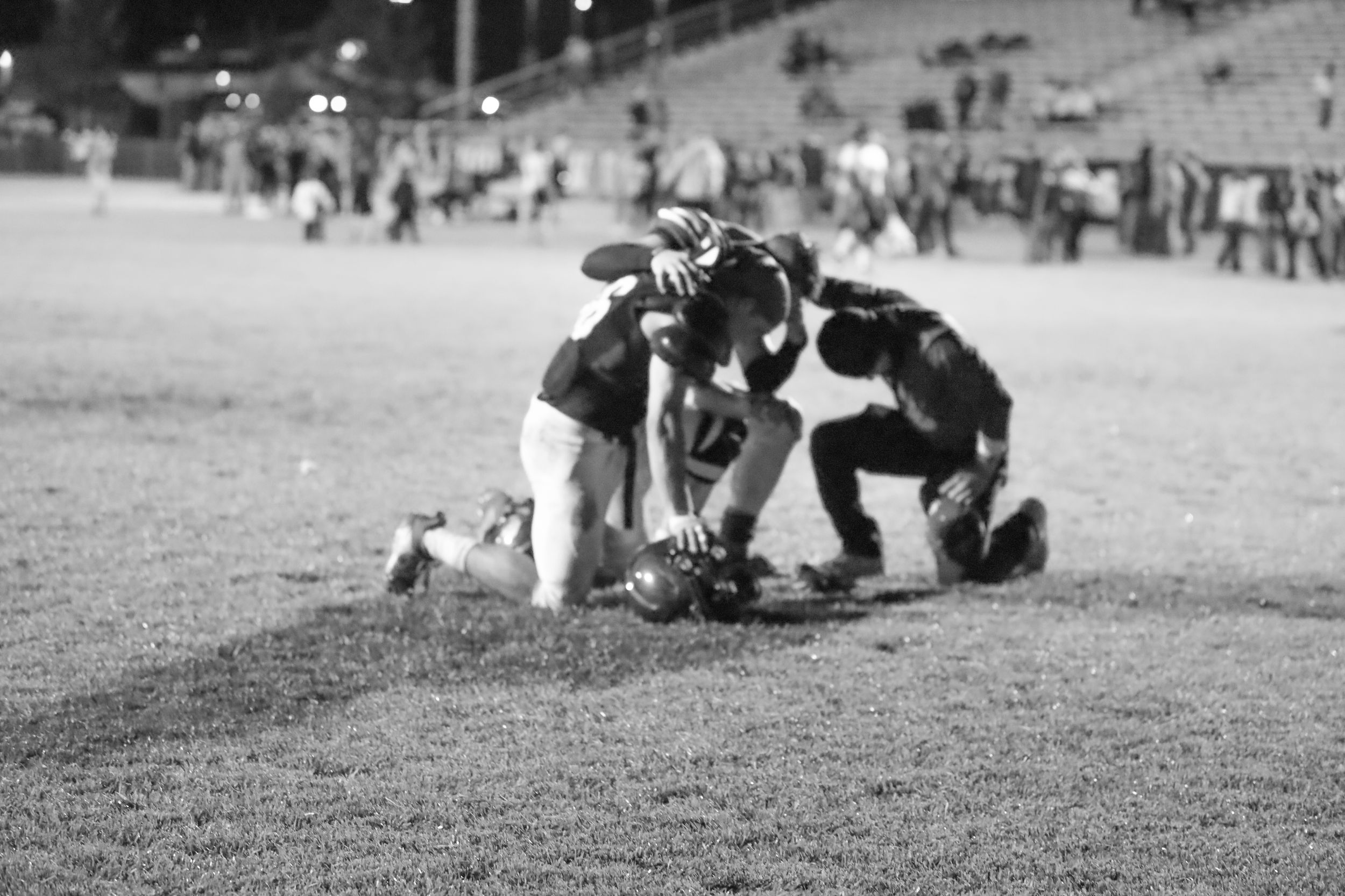 Black and white photo of football players on ground after play during night game on field.