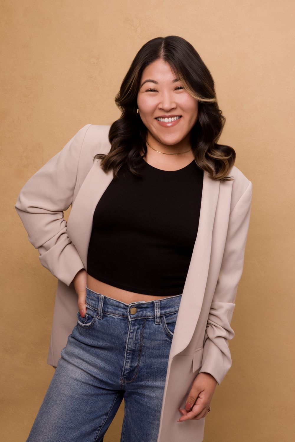 A person in a beige blazer and black top poses against a tan background in a casual professional style.