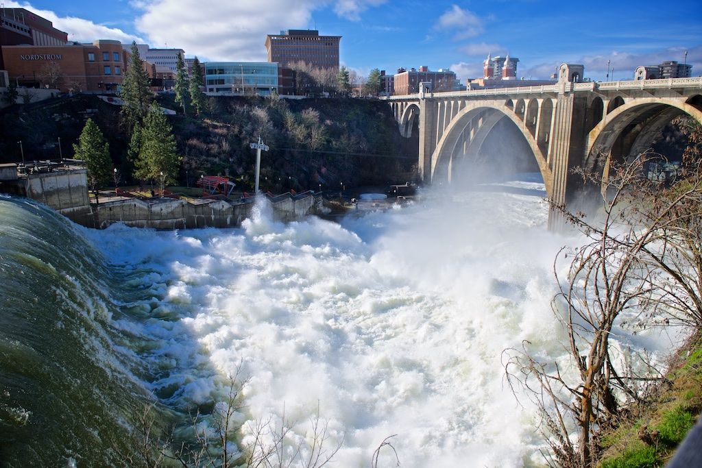 Rushing white water cascades over Monroe Street Dam beneath the Monroe Street Bridge in Spokane, Washington.