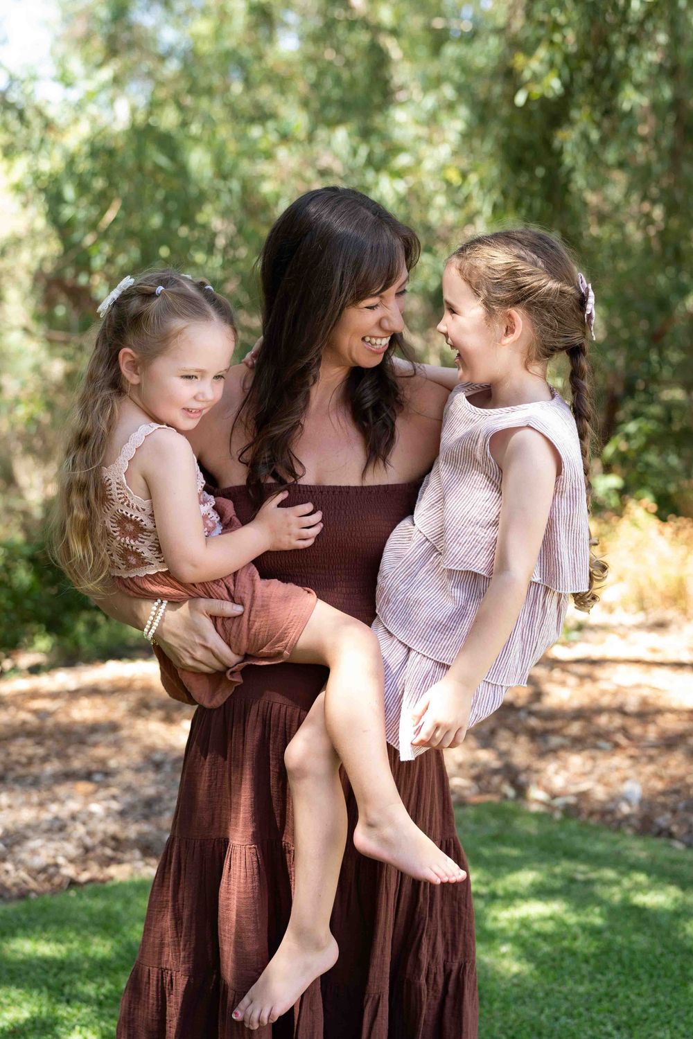 A mother holding and looking at her two young children during an outdoor family photography session in Perth