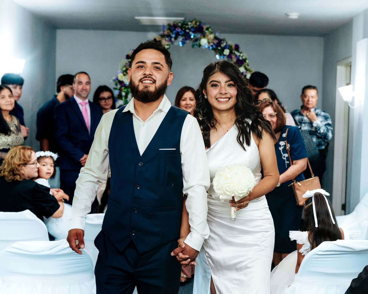 Wedding party celebrates in a modern white hallway with festive decorations and joyful dancing.