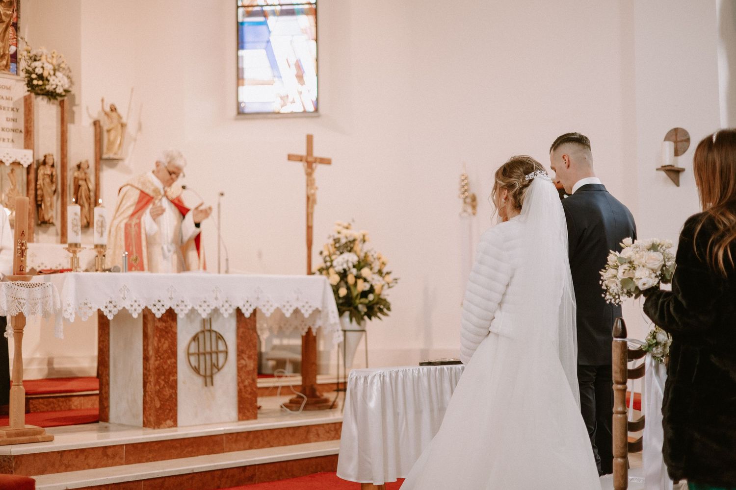 Pohľad na priebeh svadobného obradu v kostole, nevesta a ženích stoja pred kňazom počas liturgie.