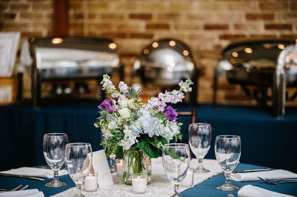 Elegant wedding reception table settings with wine glasses and floral centerpieces against exposed brick walls.