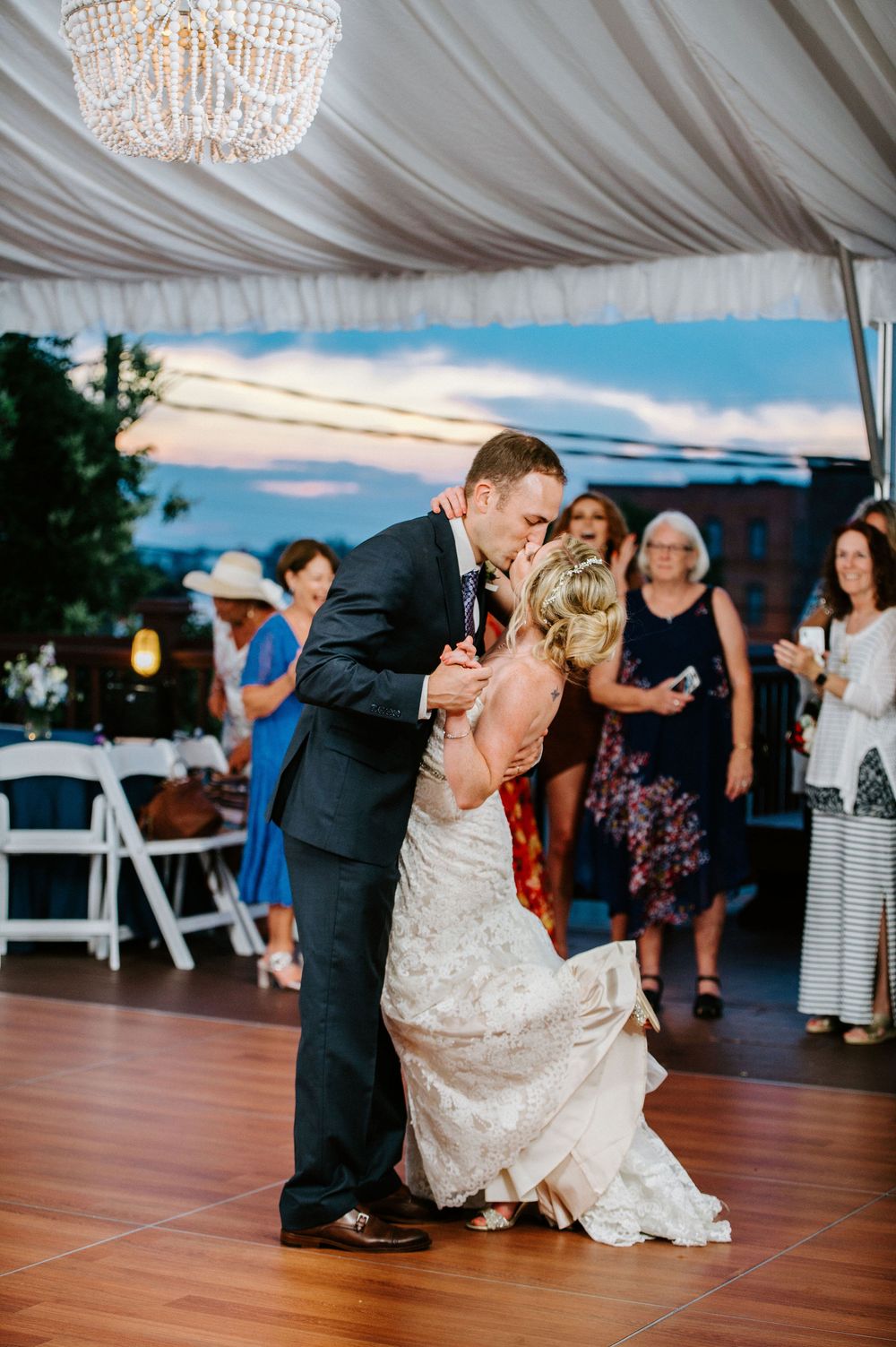 Couple dances together at a wedding reception under a white tent with elegant chandeliers.